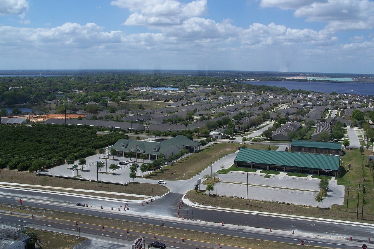 Vista aérea de bairro residencial com pomar de laranjas e um lago ao fundo.