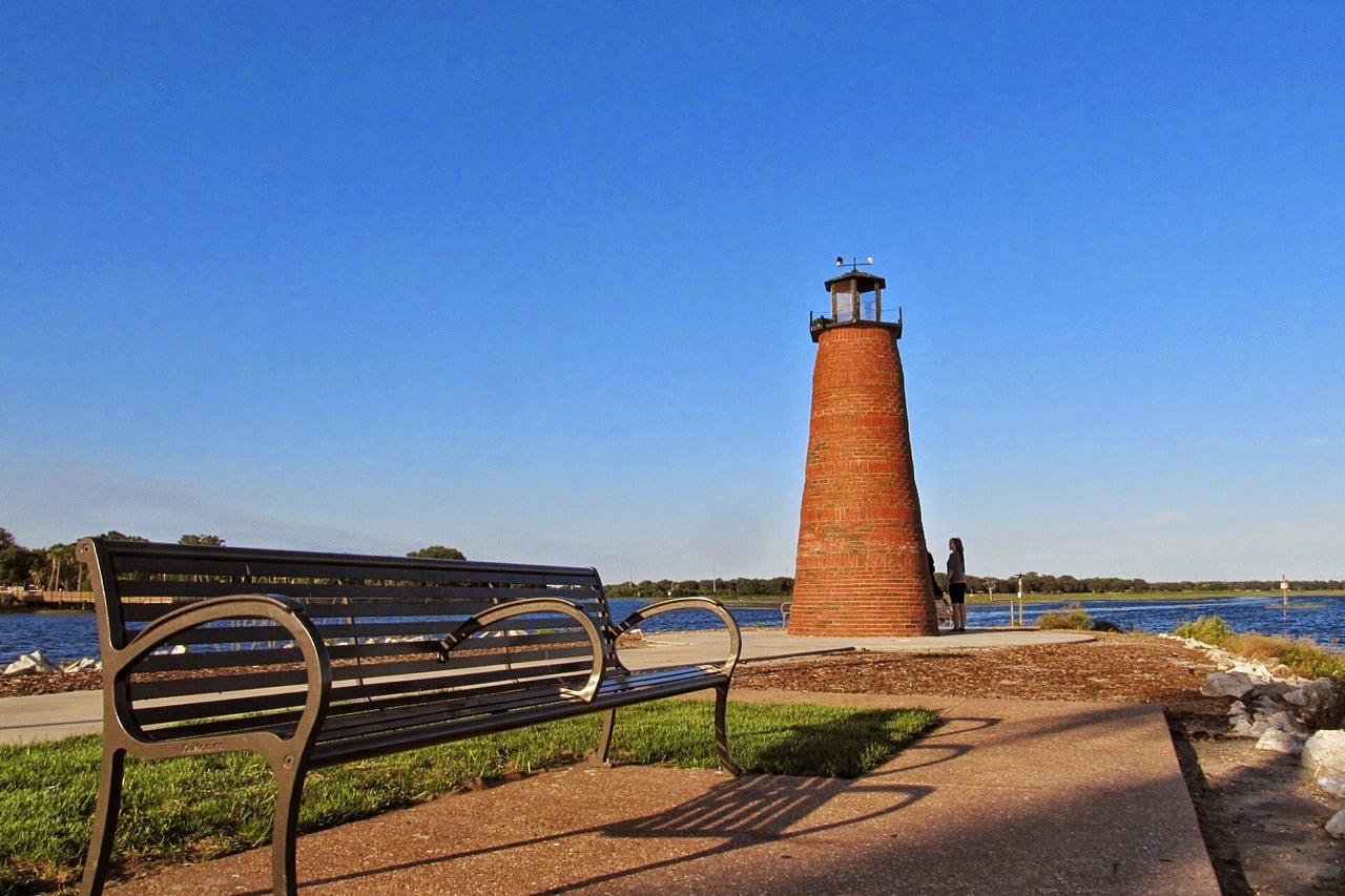 Farol de tijolo na beira do lago com um banco em primeiro plano