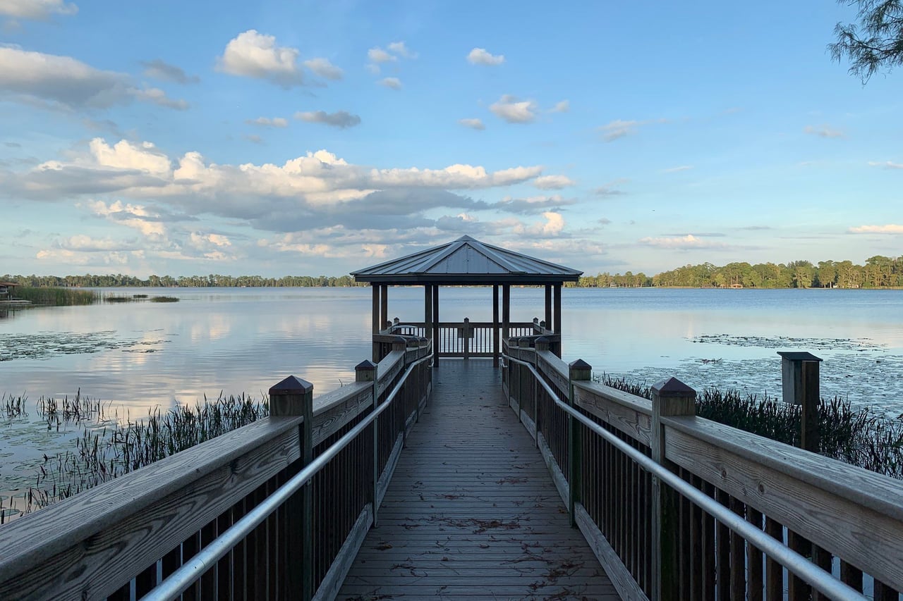 Deque de madeira com gazebo sobre um lago calmo que reflete as nuvens, na região de Lake Nona