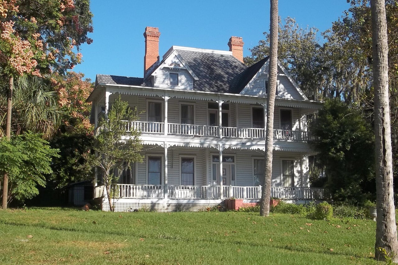 Casa histórica branca de dois andares com varandas corridas e chaminés de tijolo, cercada de gramado e árvores, em Oviedo