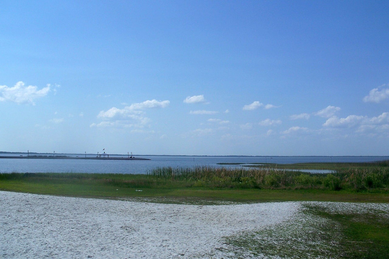 Areia clara e capim na beira do lago, com o lago aberto ao fundo