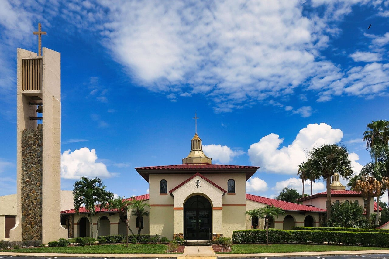 Igreja católica St. Thomas Aquinas em St. Cloud, com fachada clara, telhado vermelho, campanário e palmeiras sob céu azul
