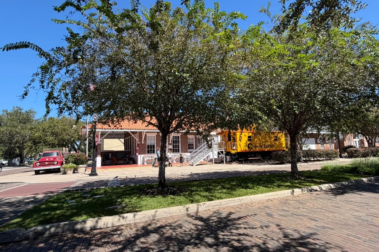 Vagão ferroviário amarelo junto a um prédio de telhado laranja, sob árvores, no centro de Winter Garden