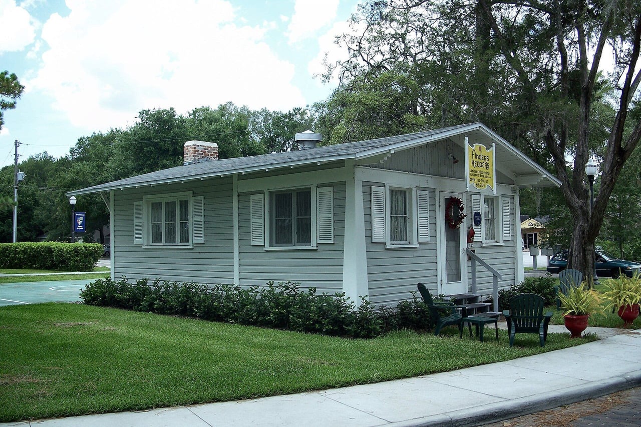Chalé de madeira cinza com venezianas brancas, gramado e cadeiras de jardim verdes no centro histórico de Windermere